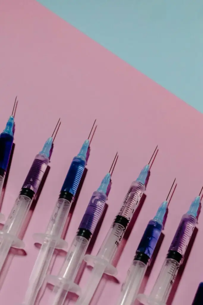 Row of syringes with colored liquids arranged diagonally on a pink background.