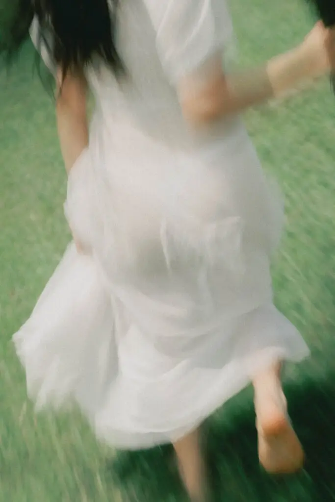 Blurry image of a person in a white dress moving outdoors on grass, captured in motion.