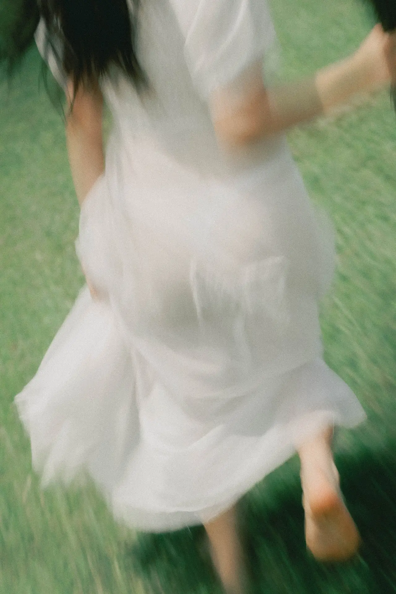 Blurry image of a person in a white dress moving outdoors on grass, captured in motion.