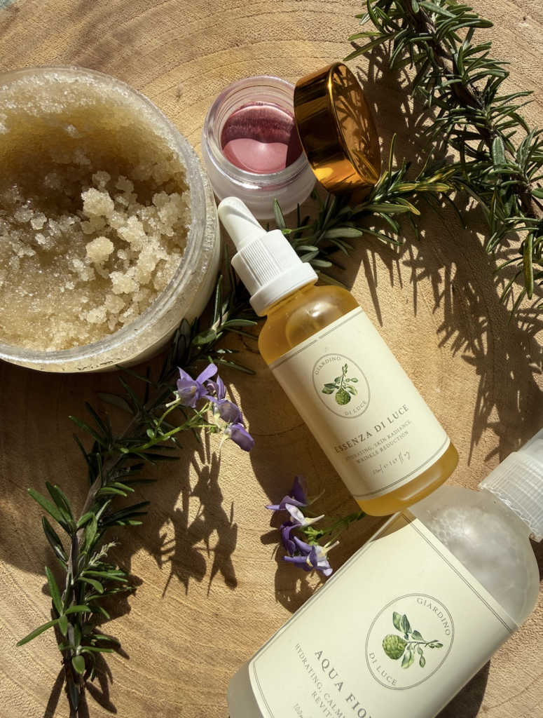 Oil and scrub skincare setup with a dropper bottle, jar of sugar scrub, and sprigs of rosemary on a wooden surface.