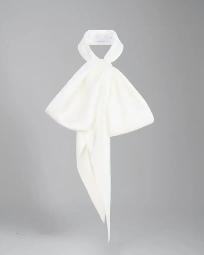 White silk scarf tied into a large bow, hangs gracefully against a light gray background (fashion accessory)