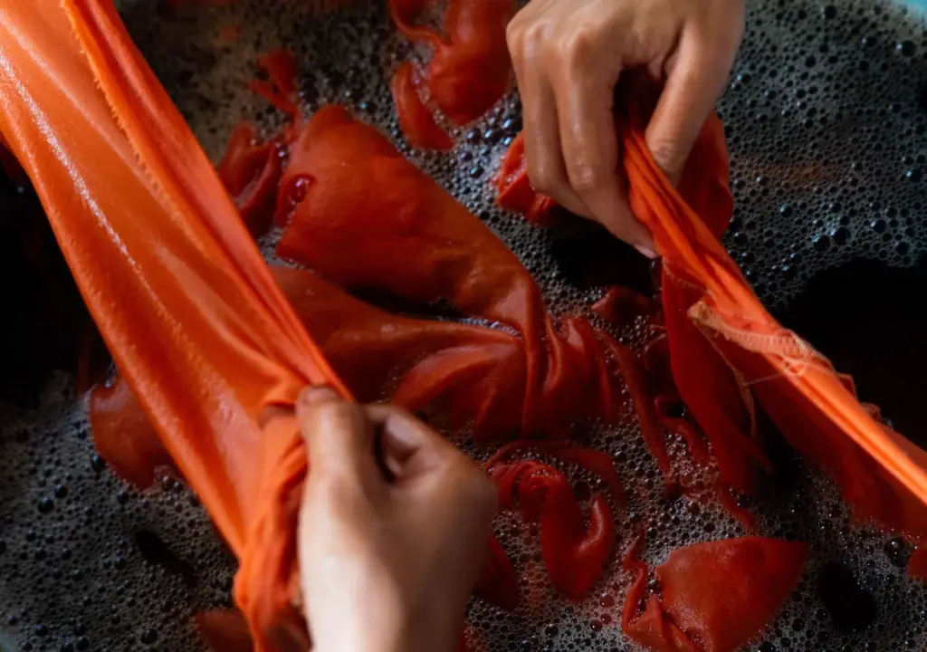 Hands wringing a bright orange fabric in foamy soapy water.